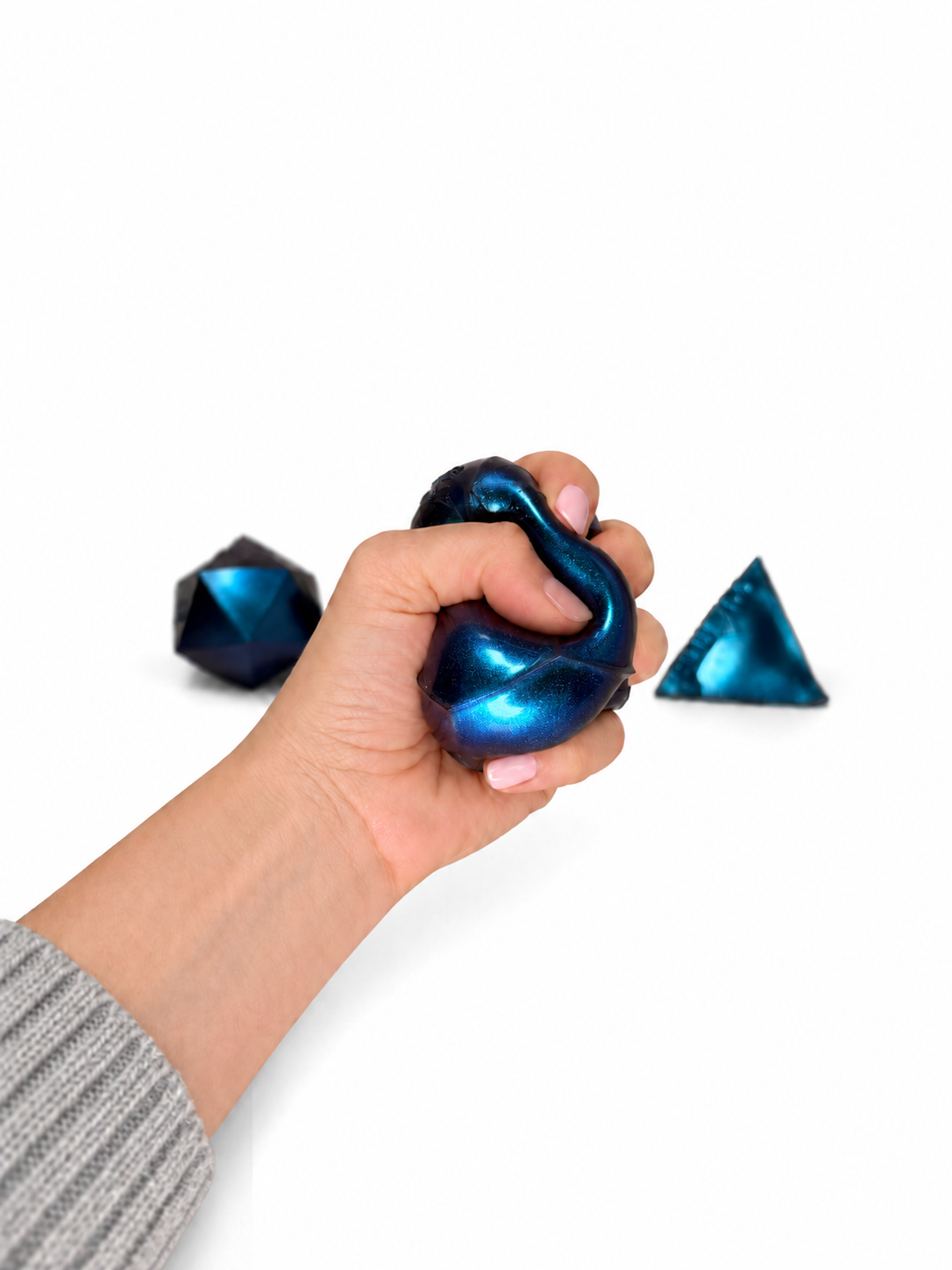 A hand squeezing a teal PolySquish Discovery Series #2 shape, with two more shapes beside it