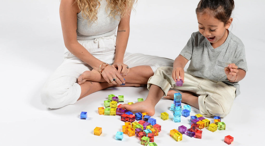An adult and child playing with colourful translucent Plato's Cubes on the floor